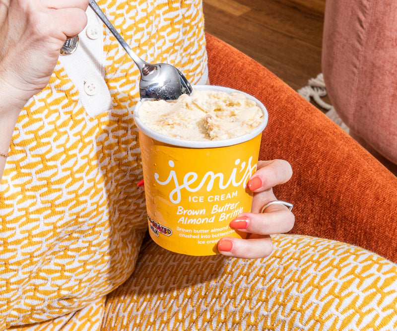 Close up of a woman's hands holding a spoon and pint of Jeni's Brown Butter Almond Brittle ice cream.